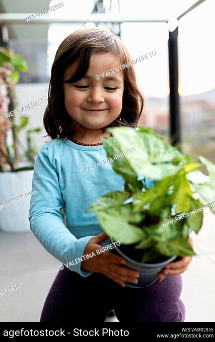 Portrait of happy little girl on balcony looking at potted plant