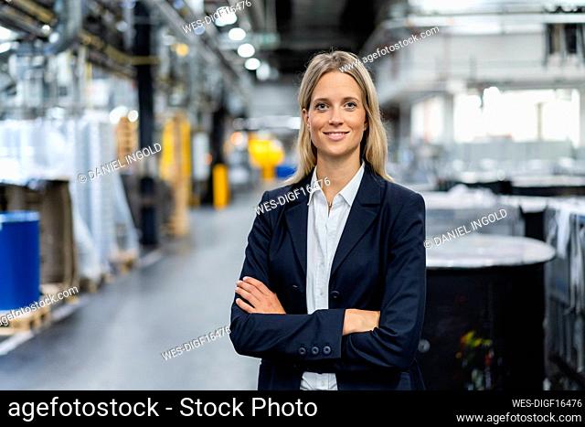 Young businesswoman with arms crossed standing at industry
