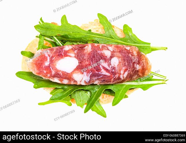 top view of open sandwich with fresh bread, cured sausage and green arugula leaves isolated on white background