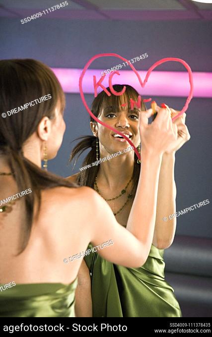 African woman drawing lipstick heart on mirror