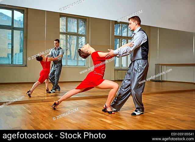beautiful couple dancing tango. young woman in red dress and man in suit practicing in dancing studio mirror room. copy space