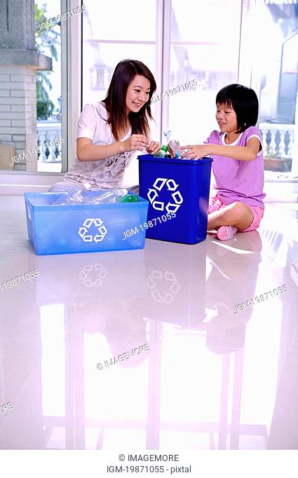 Mother with a child sitting on the floor and putting empty bottle into the recycling bin
