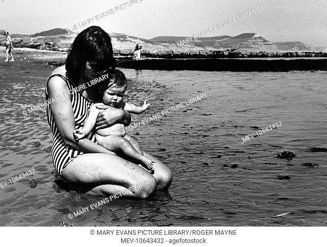 A mother and child at the seaside, on a wet beach with the tide going out