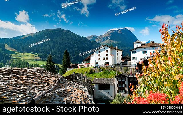 Spluegen, Grisons / Switzerland - 29 September 2019: picturesque mountain village with white stone houses and stone roofs and fall color foliage