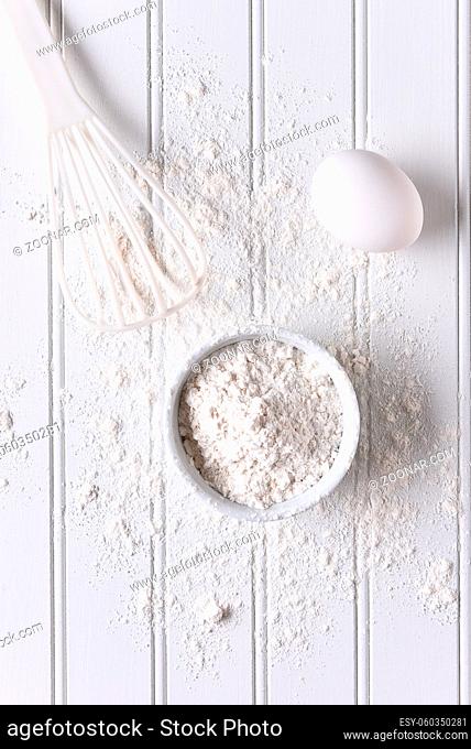 White baking still life. Top view of items for baking: eggs, flour and a whisk on a white beadboard surface