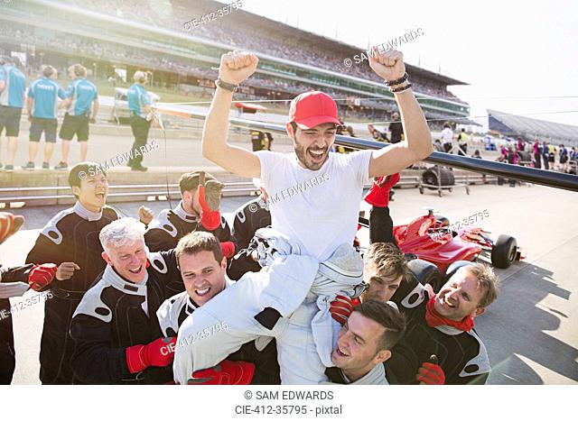 Formula one racing team carrying driver on shoulders, celebrating victory on sports track