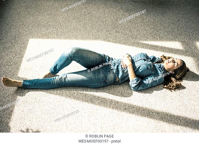 Young woman lying on carpet in the living room enjoying sunlight