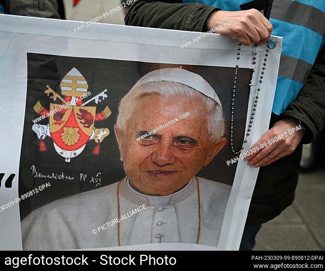 09 March 2023, Hesse, Frankfurt/Main: A man holds a banner with a portrait of the late Pope Emeritus Benedict XVI and a rosary on the sidelines of the synodal...