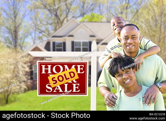 Happy african american family in front of sold real estate sign and house