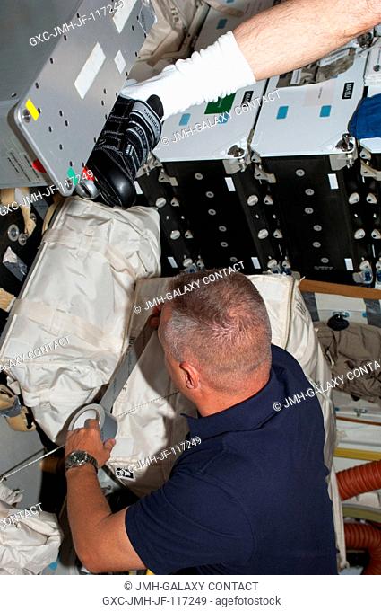 NASA astronaut Doug Hurley, STS-135 pilot, tapes up a supply bag on the middeck of the space shuttle Atlantis while the spacecraft was docked with the...