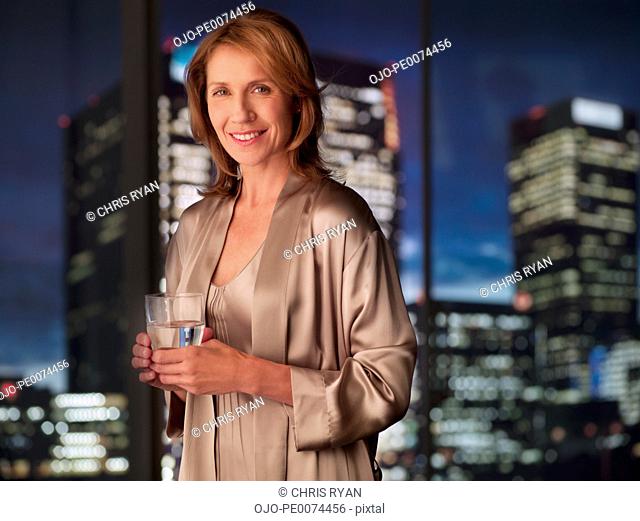 Woman in nightgown drinking with cityscape in background