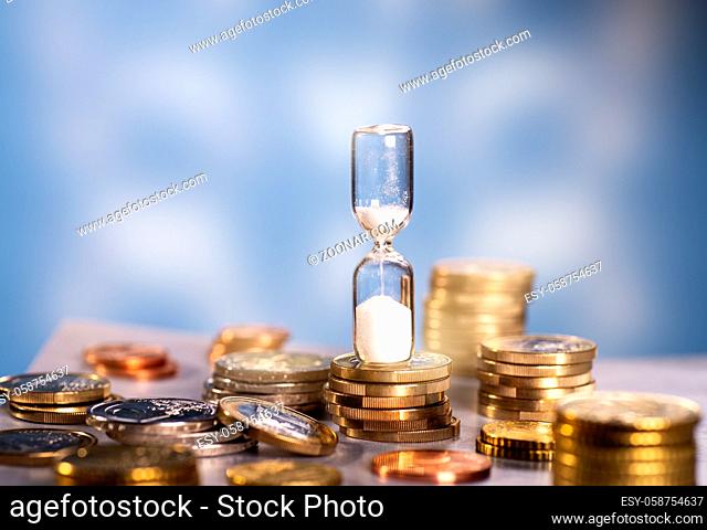 Sand rinnt durch eine Sanduhr, die auf einem Tisch mit verschiedenen Münzen steht