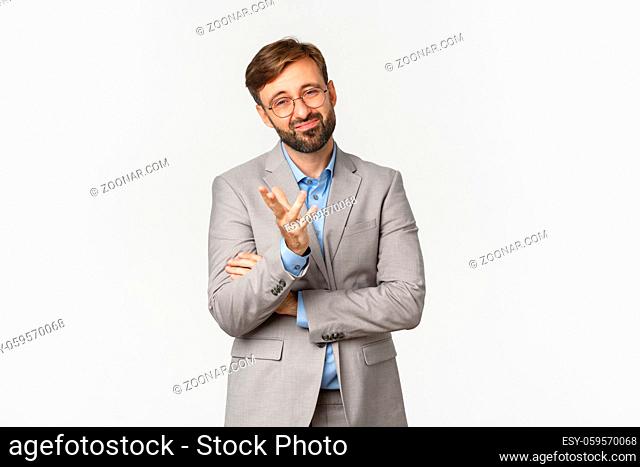 Portrait of doubtful businessman with beard, wearing glasses and suit, grimacing and looking skeptical, standing indecisive over white background