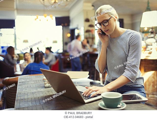Creative businesswoman talking on cell phone and using laptop in cafe
