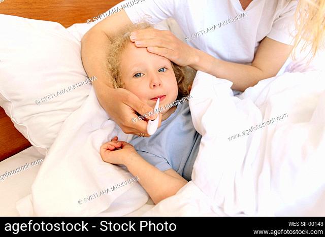 Mother measuring body temperature of daughter in bedroom