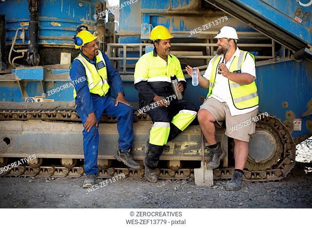 Colleague workers at quarry sitting on machine, taking a break