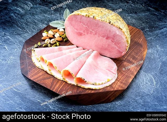 Modern style traditional German boiled Christmas ham with exotically spices and sage offered as close-up on a wooden design board with copy space