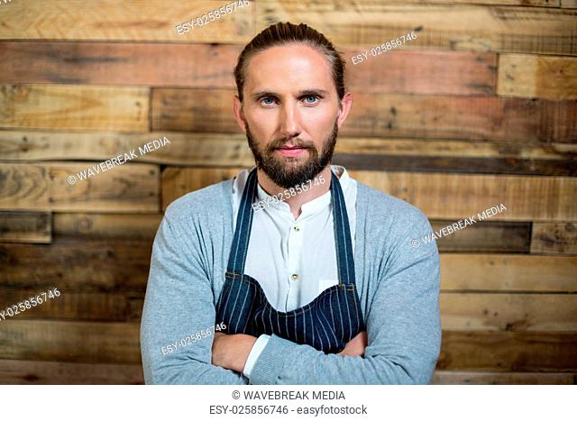 Portrait of waiter standing with arms crossed against wooden wall
