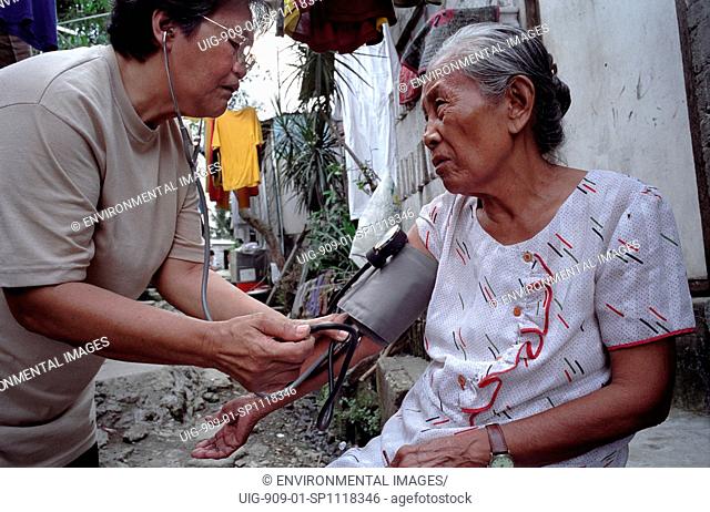 HEALTHCARE, PHILIPPINES. Manila. Payatas. Voluntary health worker checking the blood pressure of elderly lady.