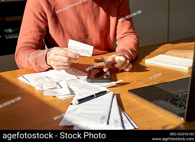 Hands of man with financial bills calculating on smart phone at desk