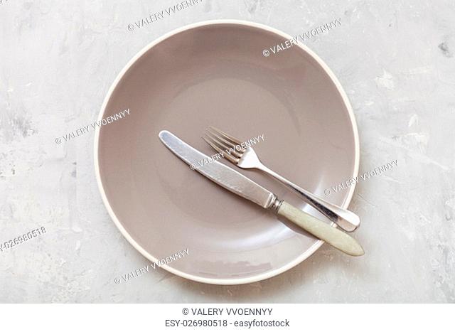food concept - top view of gray plate with parallel knife, spoon on gray concrete surface