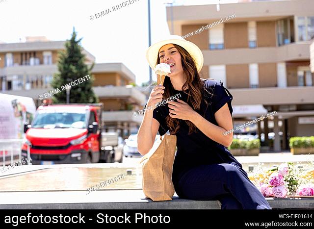 Woman in sun hat eating ice cream while sitting on seat