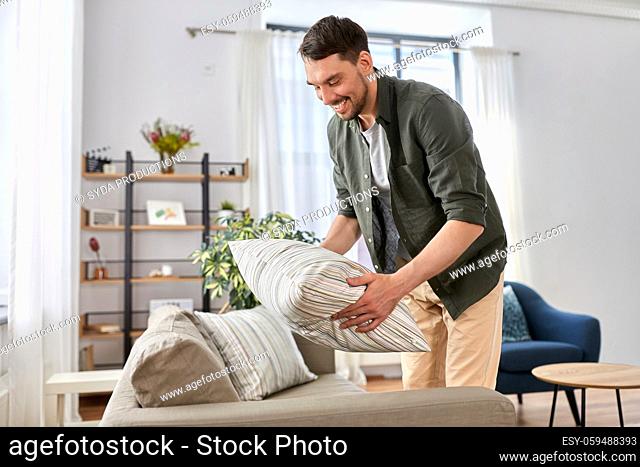 happy smiling man arranging sofa cushions at home