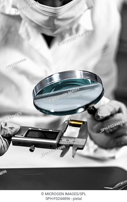 Forensic science analyst using magnifying glass, examining bullet casing