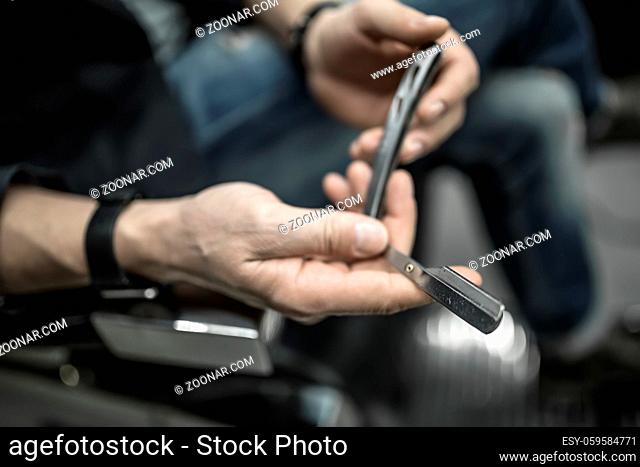 Straight blade in the hands of a man on the blurry background of his body. Closeup photo on the wide aperture. Horizontal