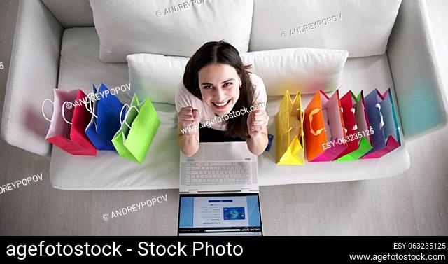 Young Woman Sitting On Sofa Shopping Online With Shopping Bags