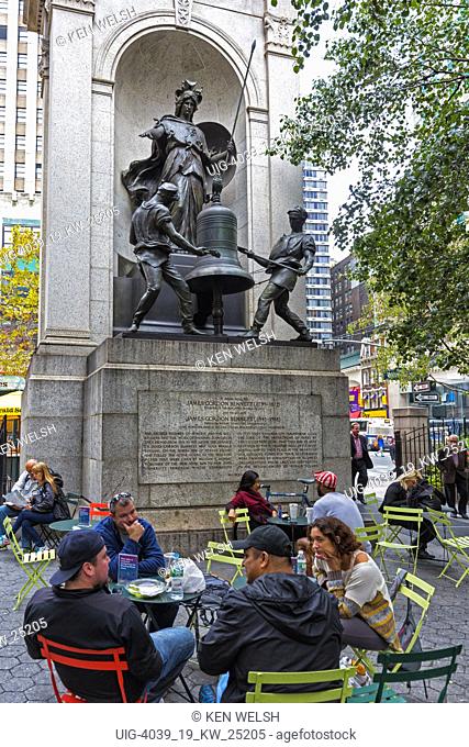 Herald Square, New York City, New York State, USA. People relaxing in outdoor cafe tables .  Behind them the memorial to James Gordon Bennett, 1795-1872
