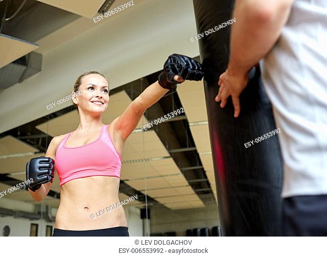 sport, fitness, lifestyle and people concept - smiling woman with personal trainer boxing punching bag in gym