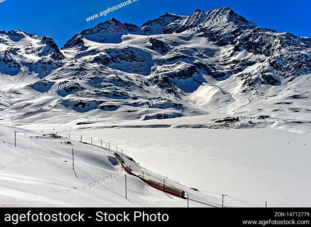 Bahnlinie der Rhätischen Bahn mit dem Bernina Express in der winterlichen Alpenlandschaft am Berninapass, Engadin, Graubünden