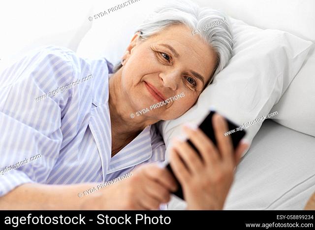 happy senior woman with smartphone in bed at home