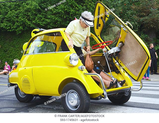 A BMW Isetta 250 being driven in a parade for the Comox Aquatic Days festival has stopped and is showing how a passenger gets out
