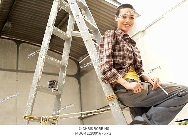Female interior decorator sitting on ladder in work site portrait low angle view
