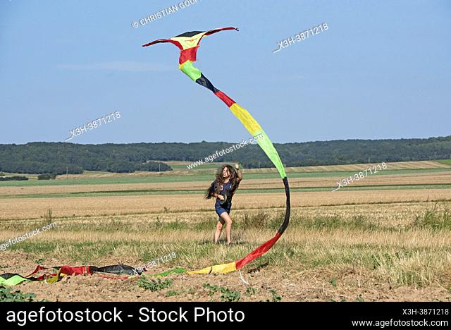 Young girl in denim shorts and blue shirt flying a Chinese kite in a flat landscape in Centre-Val de Loire region, France