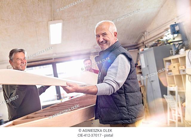 Portrait smiling senior male carpenter lifting wood boat in workshop