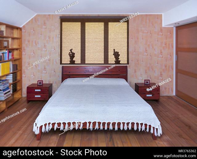 Bedroom interior with large bed, furniture and bedside tabel. Shadows on roller blind