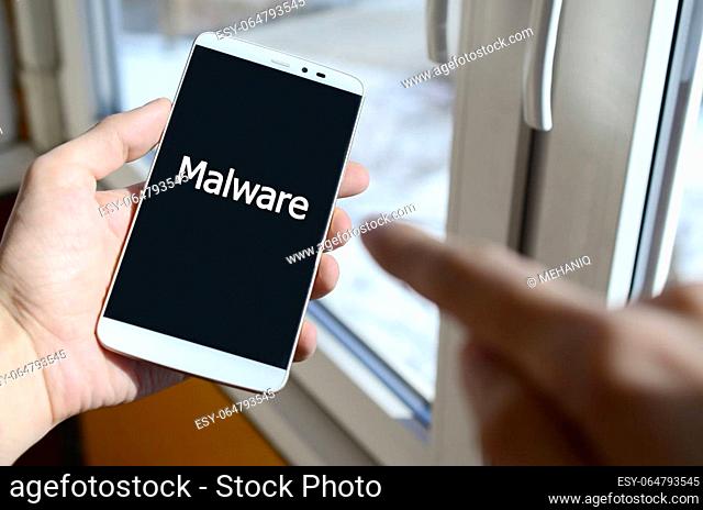 A person sees a white inscription on a black smartphone display that holds in his hand. Malware