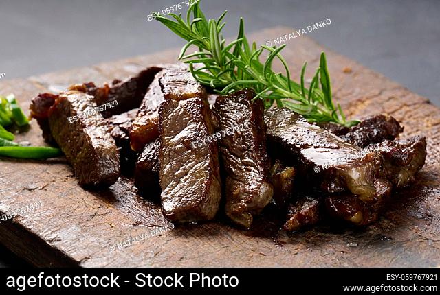 roasted piece of beef ribeye cut into pieces on a vintage brown chopping board, rare doneness. Appetizing steak