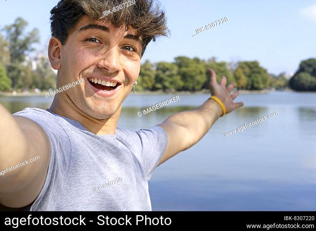 Active handsome young Caucasian man taking selfie showing around at a lake. Outdoor adventure concept