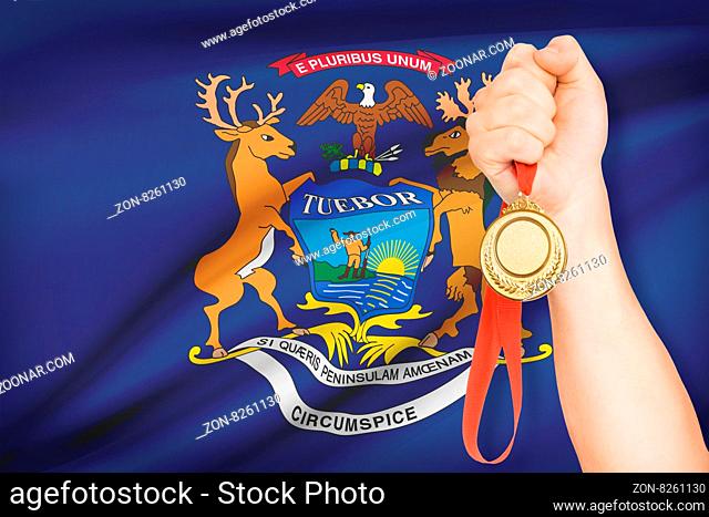 Sportsman holding gold medal with State of Michigan flag on background. Part of a series