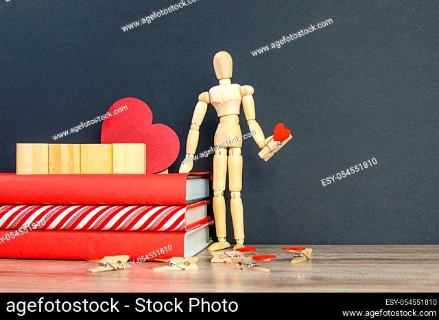 A stack of red books on which there are 4 wooden cubes, and next to there is a figure of a wooden man with a pin in the shape of a heart in his hand
