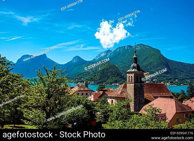 View of houses and belfry with blue sky mountains landscape on background, in the village of Talloires. A lovely village next to the Lake of Annecy