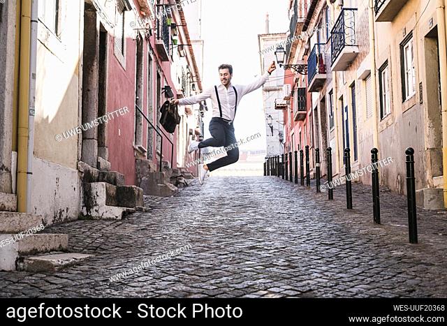 Carefree young man jumping in the old town, Lisbon, Portugal