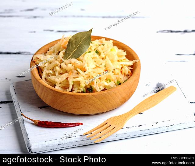 salad from sauerkraut, carrots and green onions in a brown wooden bowl on a white board