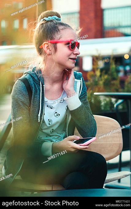 Teenage girl having fun using smartphone sitting in center of town