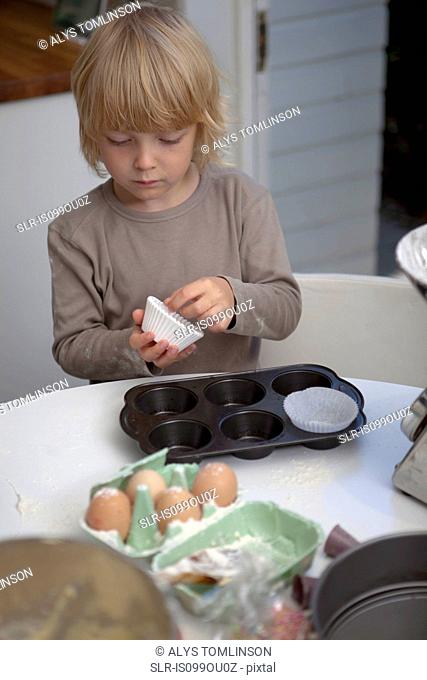 Boy putting cake cases into cupcake tray