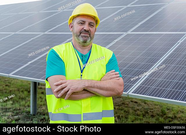 Engineer in hardhat standing by arms crossed at solar station